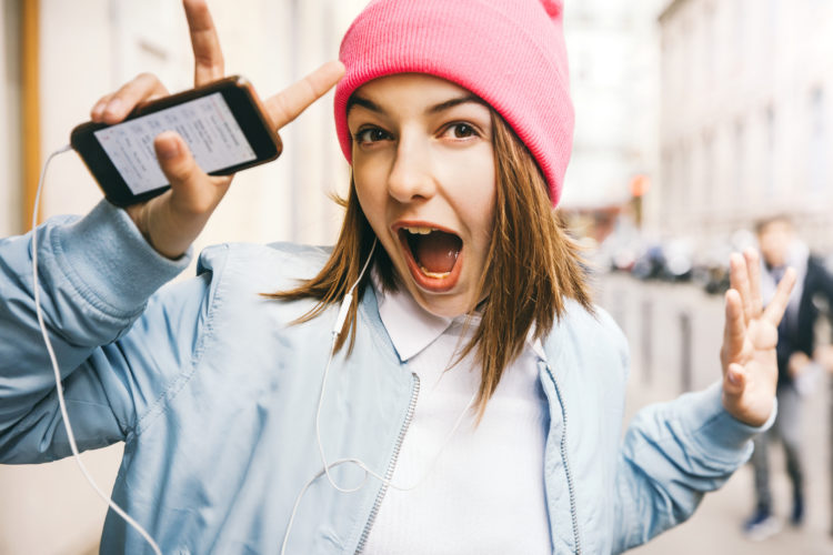 Teenager girl listening to music with headphones from a smart phone in the street of Paris.